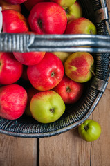 Top view of fresh garden red and green apples in a gray basket on a wooden background. Dark rustic style.