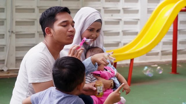 Video footage of cheerful muslim parents and their children playing soap bubbles at the park, shot outdoors