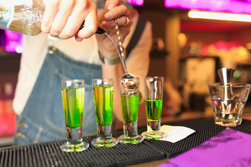 The barman's hands pouring absinthe into one of the stacks standing on the counter