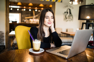Pretty brunette using her laptop in a coffee shop and look at screen