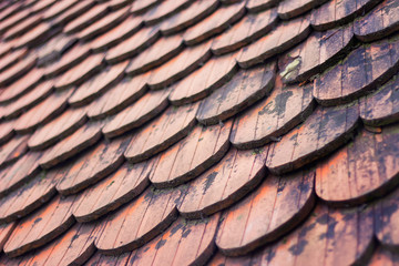 Roof covered with red old rounded wooden roof tiles diagonal view.