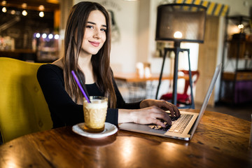 Charming beautiful young woman using laptop computer. Female working on laptop at bar in cafe