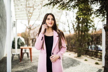 Cheerful woman talking on the phone in the street wearing a pink coat jacket