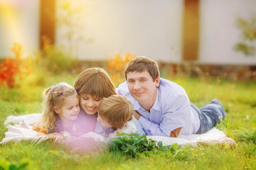 Fototapeta premium Big family is lying on a plaid in a green meadow. Mom and children are looking at some insect