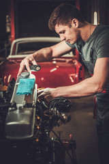 Fototapeta na wymiar Mechanic working on classic car engine in restoration workshop