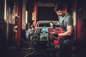 Fototapeta na wymiar Mechanic working on classic car engine in restoration workshop