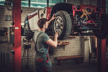 Fototapeta na wymiar Mechanic working on classic car wheels and suspension in restoration workshop
