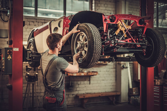 Mechanic working on classic car wheels and suspension in restoration workshop