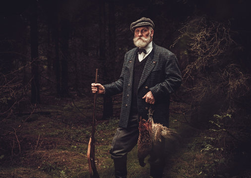 Senior hunter with a shotgun and pheasants in a traditional shooting clothing