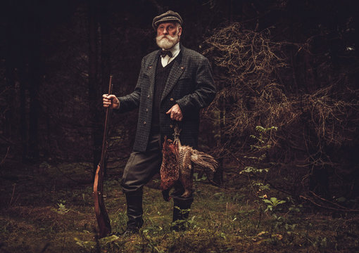 Senior hunter with a shotgun and pheasants in a traditional shooting clothing