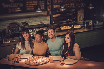 Cheerful multiracial friends eating in pizzeria.