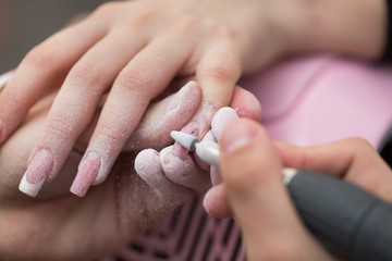 Closeup shot of master uses an electric machine to remove the nail polish during manicure in the...
