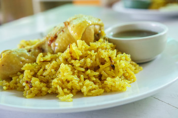 Chicken biryani (chicken rice curry with coconut) with spicy sauces on white dish in vintage white wooden table. For food.
