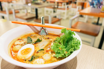 spicy noodle soup with egg, fish ball, vegetable, spoon and chopsticks in white bowl on wood table.