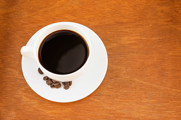 Coffee in white cup and saucer on brown wooden background with copy space.