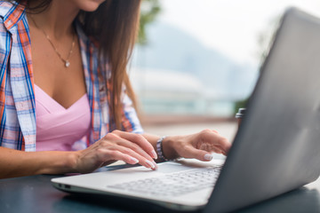 Close up shot of female hands typing on a laptop keyboard. Young woman studying and working in the park