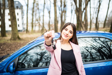 Beautiful young girl with car key in hand in front of her new car on road.