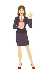 Businesswoman holding a piggy bank and showing a okay hand sign
