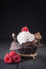 Chocolate cake is decorated with raspberries and cream on a wooden table.