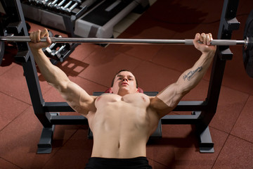 Brutal athletic man pumping up muscles on bench press