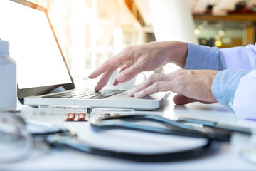 Close up of unknown female doctor sitting at the table near the window in hospital and typing at laptop computer