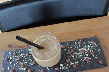 Glass of chocolade milkshake standing on a tray decorated with grated chocolade
