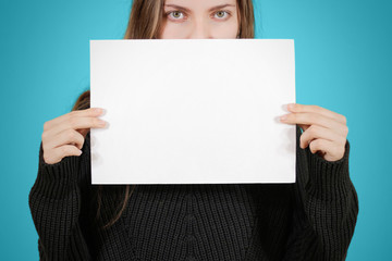 Naklejka premium Girl holding white A4 blank paper. Covers the face, mouth and nose. Eyes seen. Leaflet presentation. Pamphlet hold hands. Woman show clear offset paper. Sheet template.
