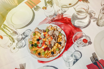 Sunlit cold plate with cheese and ham and fruit. Decorated table in the garden