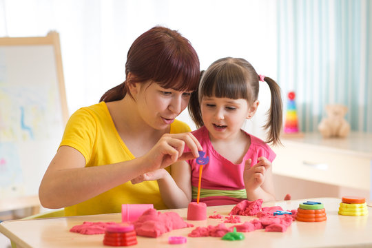 Cute little girl and mother playing with kinetic sand at home