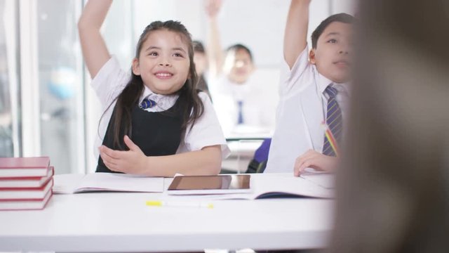  Happy school children in class listening to teacher & answering questions