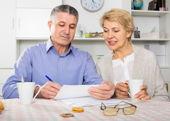 friendly mature couple at table attentively study documents