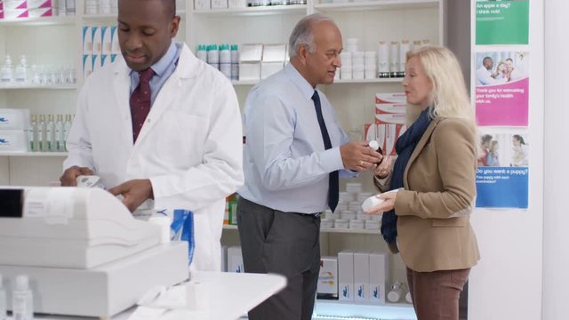  Friendly pharmacy worker serving customers & taking payment at the till