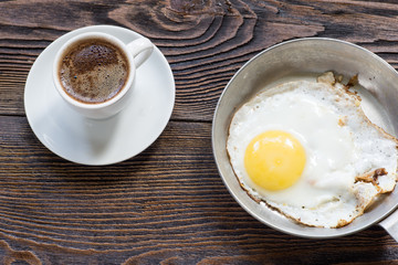 Fried egg on the pan and white  cup of coffee for breakfast.