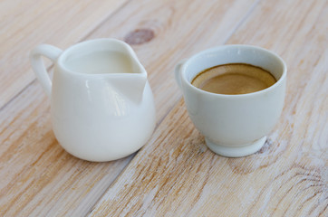 White porcelain cup of espresso and small milk jug on rustic wood table. Black coffee with milk concept.