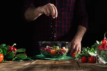 Fotobehang Man sprinkles salt salad of fresh vegetables on wooden table © kucherav