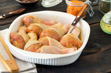 Raw chicken legs in baking dish on wooden table closeup