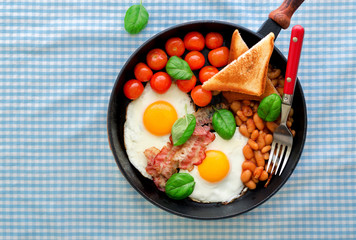 Breakfast table with fried egg, beans, tomatoes, bacon and toast