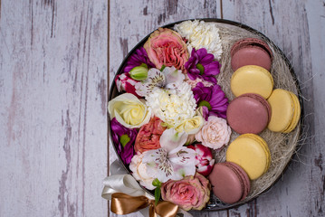 Box with fresh flowers and macaroons on wooden background