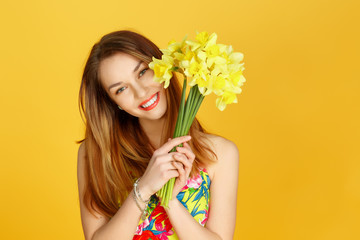 Woman holding yellow flowers and smiling against yellow wall