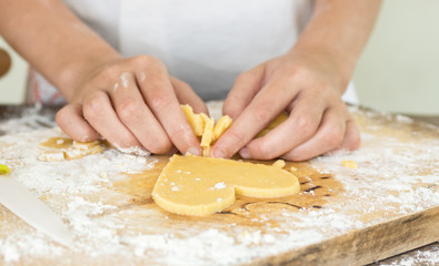 Hands cut heart shaped cookie from dough