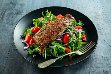 Smoked Mackerel Salad with tomato, chopped red onion, Ruccola on black plate.