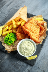British Traditional Fish and chips with mashed peas, tartar sauce on crumpled paper.