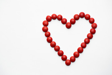 Colorful m&m button chocolate candies in the love shape on white background.