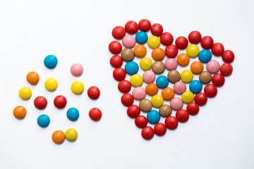 Colorful m&m button chocolate candies in the love shape on white background.
