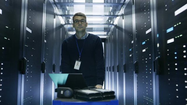 Following Shot of Server Engineer Pushing Crash Cart with Laptop, Hard Drives and Hardware Through Data Center. He Walks along Rows of Server Racks.  Shot on RED EPIC-W 8K Helium Cinema Camera.