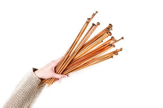 Bunch of brown bamboo wooden knitting needles in woman hand on white background. Top view