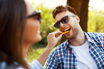 Young couple eating French fries in a park on a sunny day