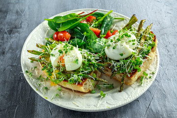 Healthy Breakfast Smashed Avocado, asparagus and poached egg on grilled toasts for breakfast served with salad and plum tomatoes