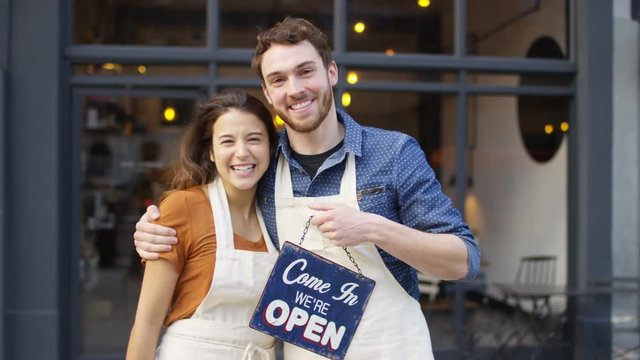  Happy owners outside cafe hold up a sign to show they are open for business. 