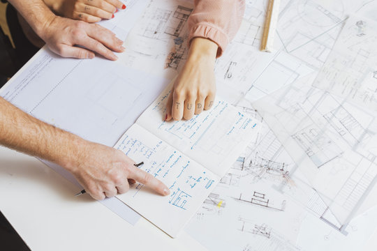 Hands of unrecognizable male and female designers working with the plan from above.